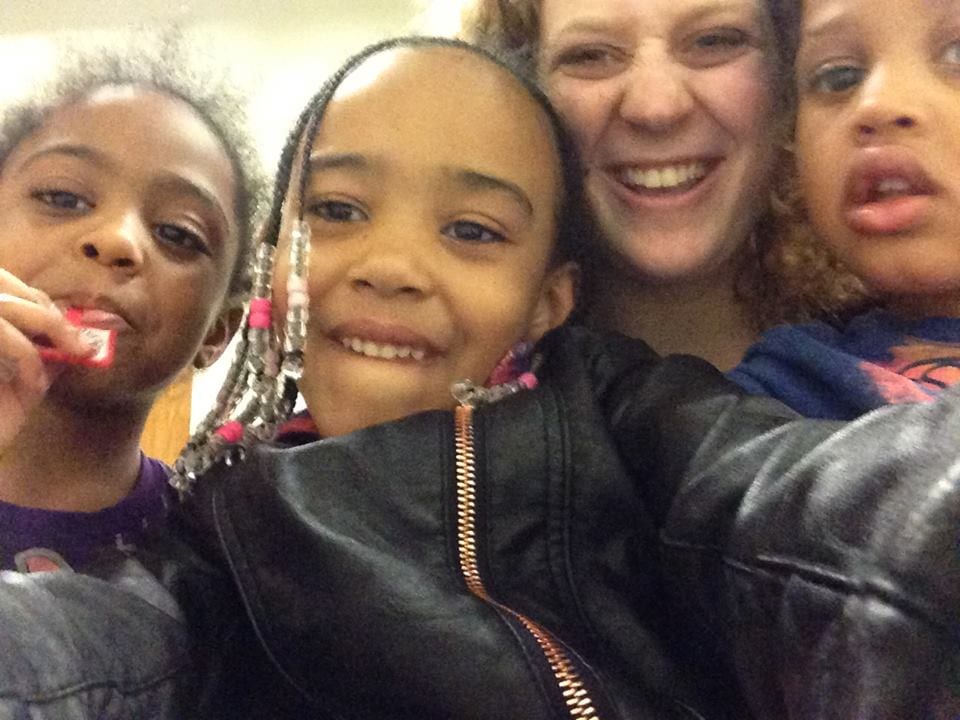 Gap year program participant and three young children smiling at the camera
